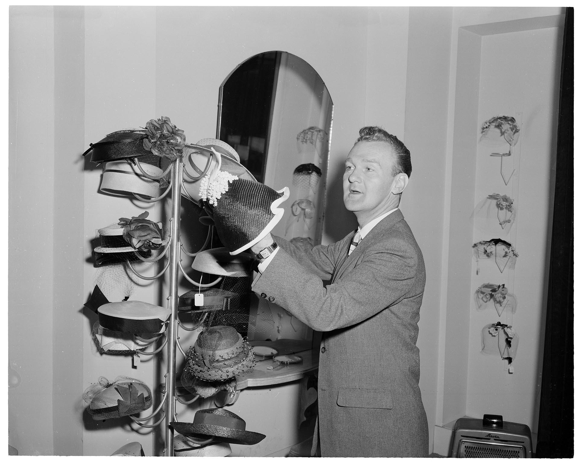 Image of John Eaton adjusting hats on display, Seattle, circa 1960