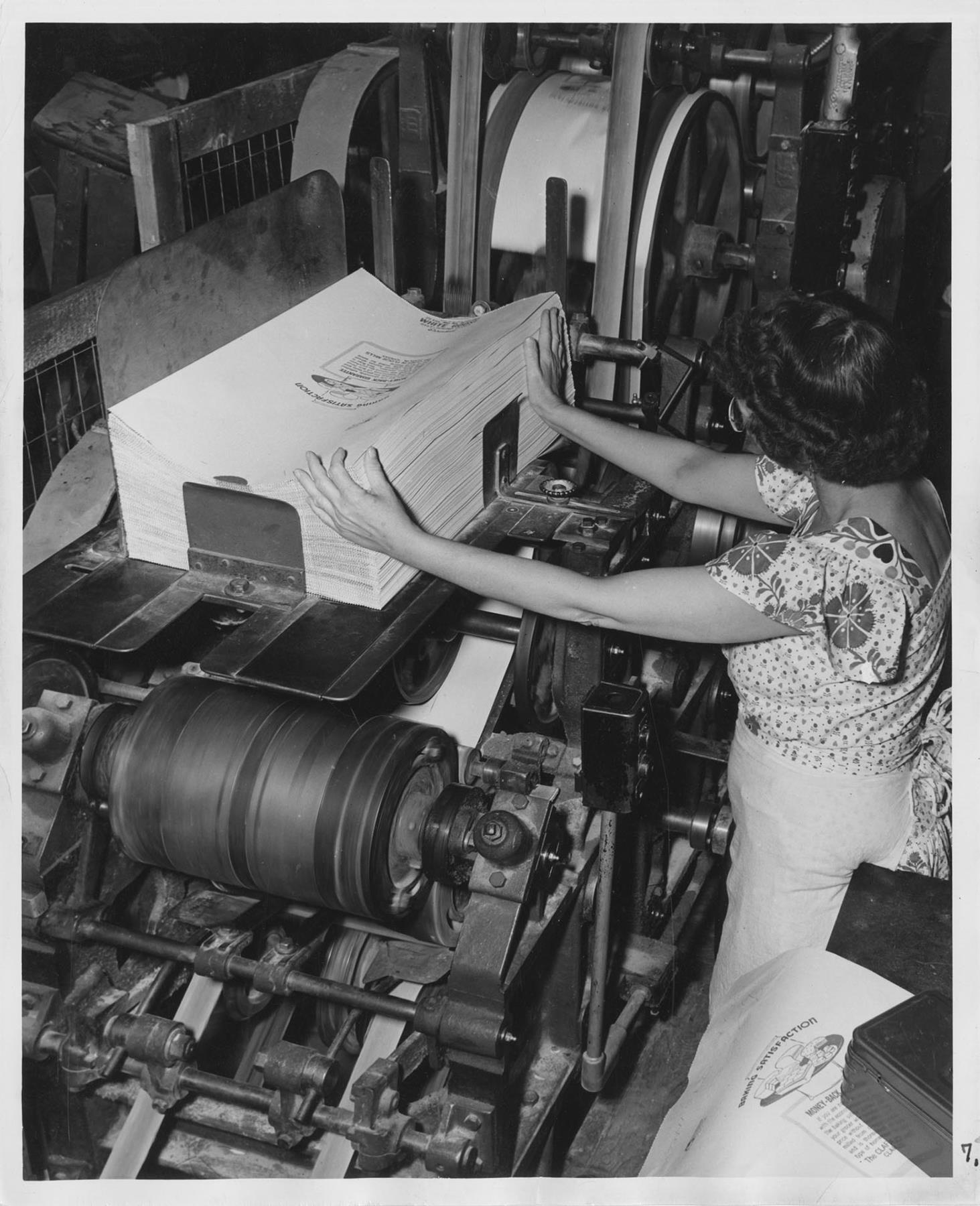 Image of Woman at Bemis Bag Co. plant loading finished bags onto machine, circa 1950