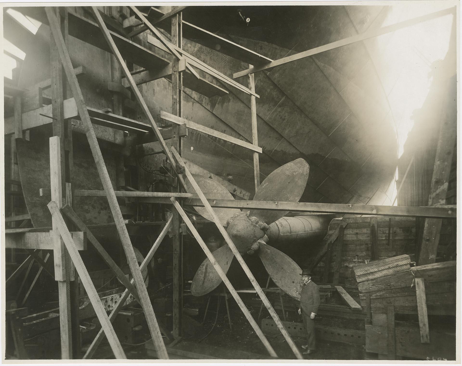 Image of Robert Moran posing near a propeller at Moran Brothers shipyard, Seattle, circa 1899
