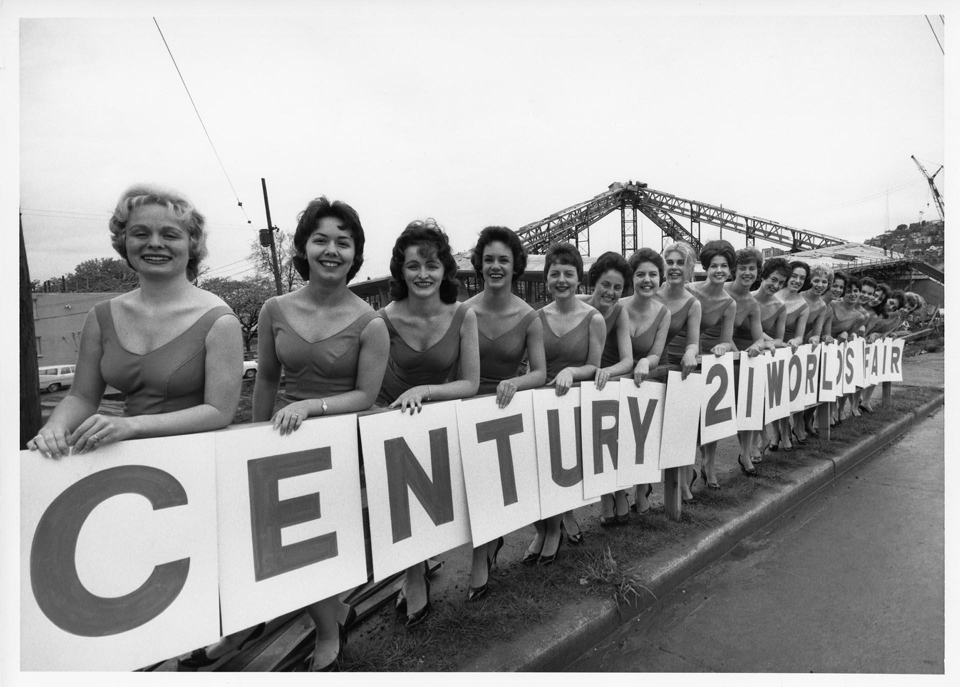 Image of Women posing with Century 21 sign during construction for the Seattle World’s Fair, 1961