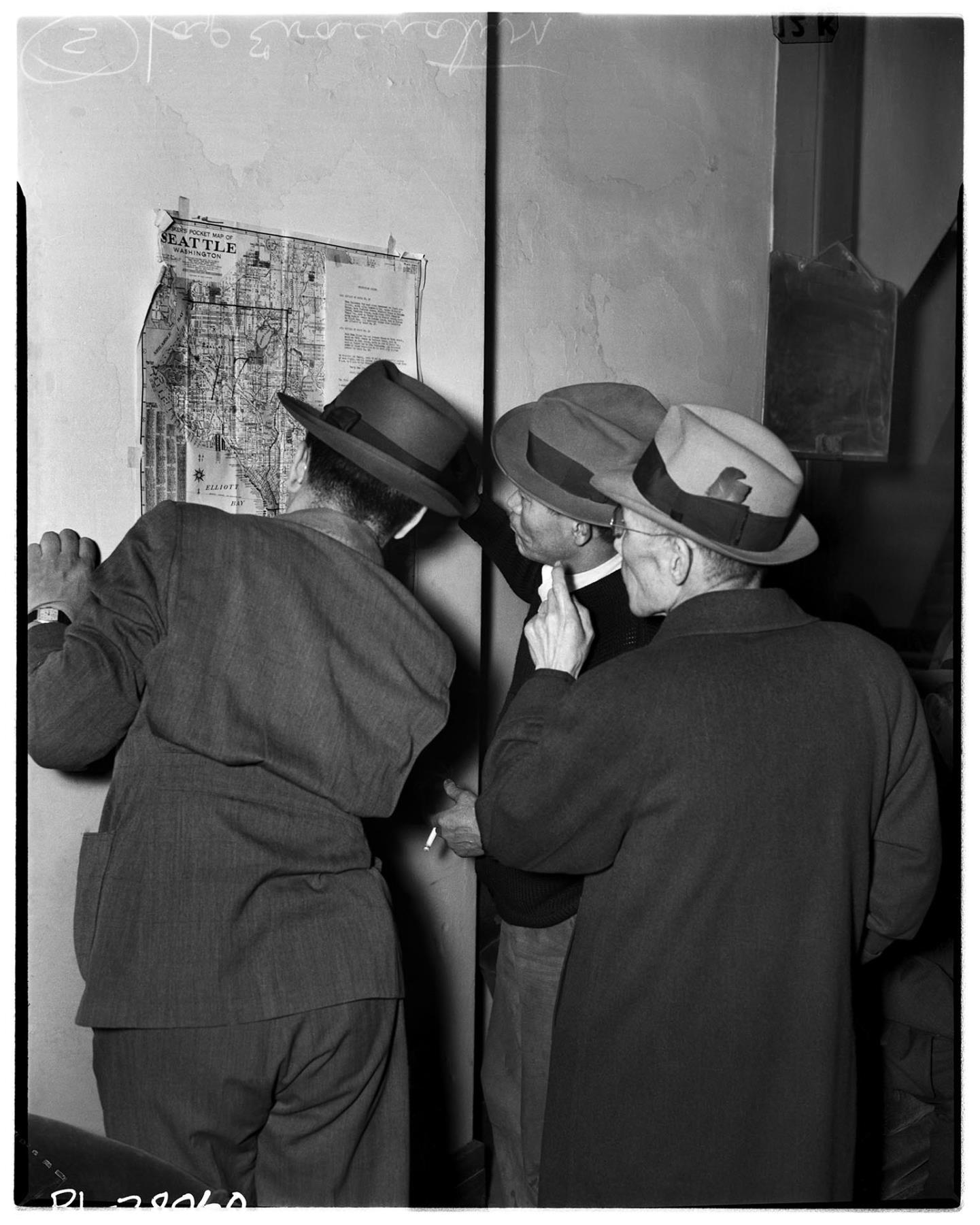 Image of Japanese American men looking at map of exclusion districts, Seattle, April 11, 1942