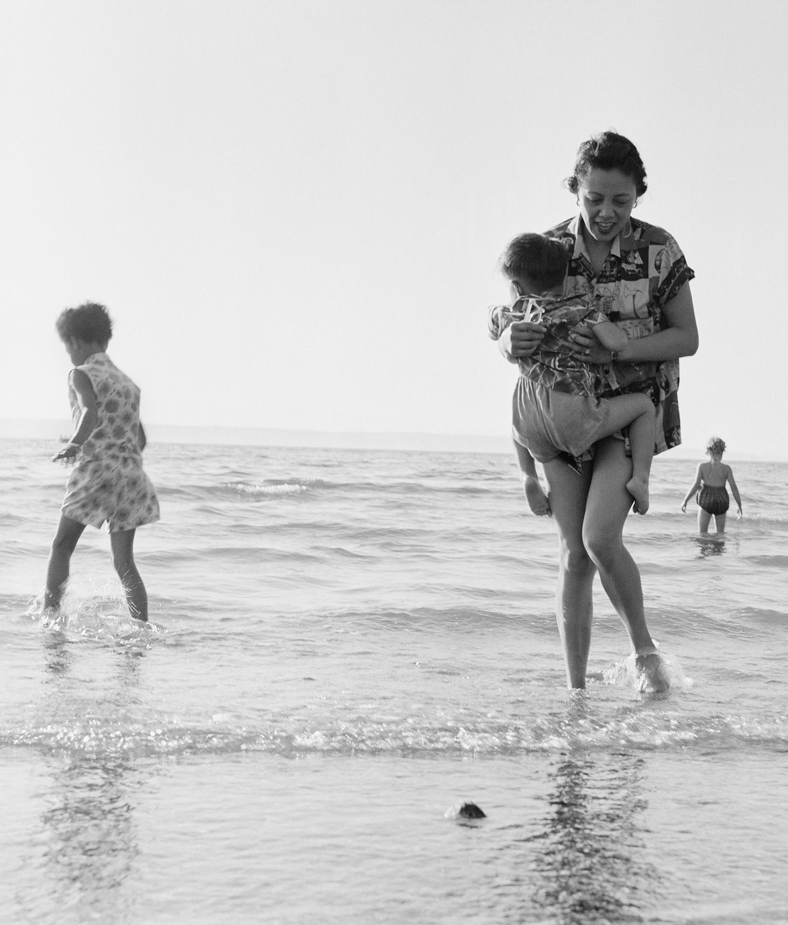 Image of Mildred Mar carrying child at beach, Des Moines, circa 1960