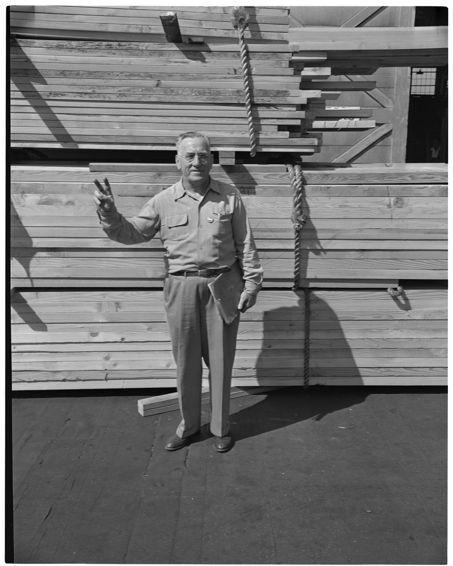 Image of Man standing on a dock with lumber, Seattle, circa 1953