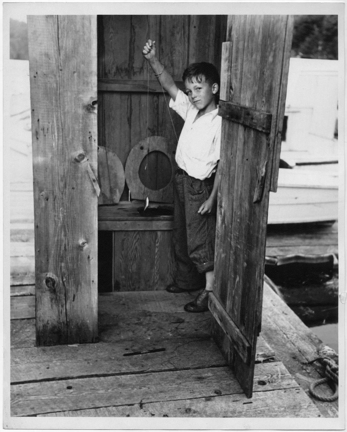 Image of Boy in outhouse, with tiny fish, circa 1956