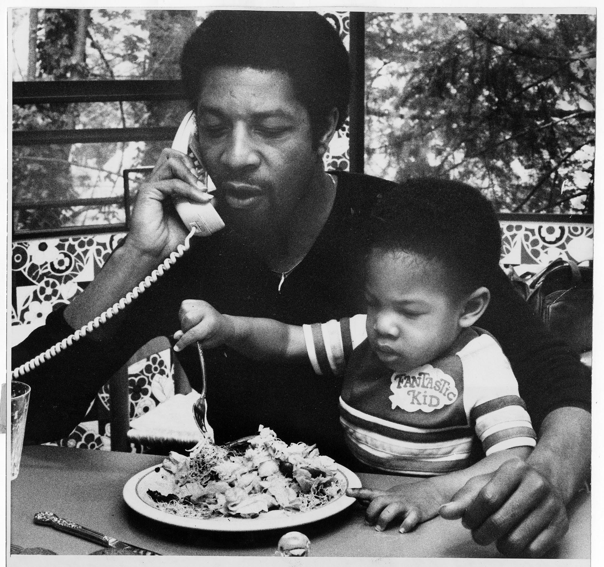 Image of Fred Brown holding son Terik during lunch at home, Seattle, July 1979