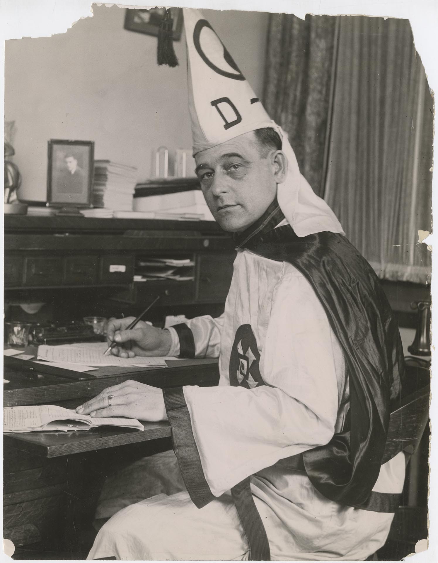 Image of Luther Powell sitting at desk in Klan robes, circa 1923