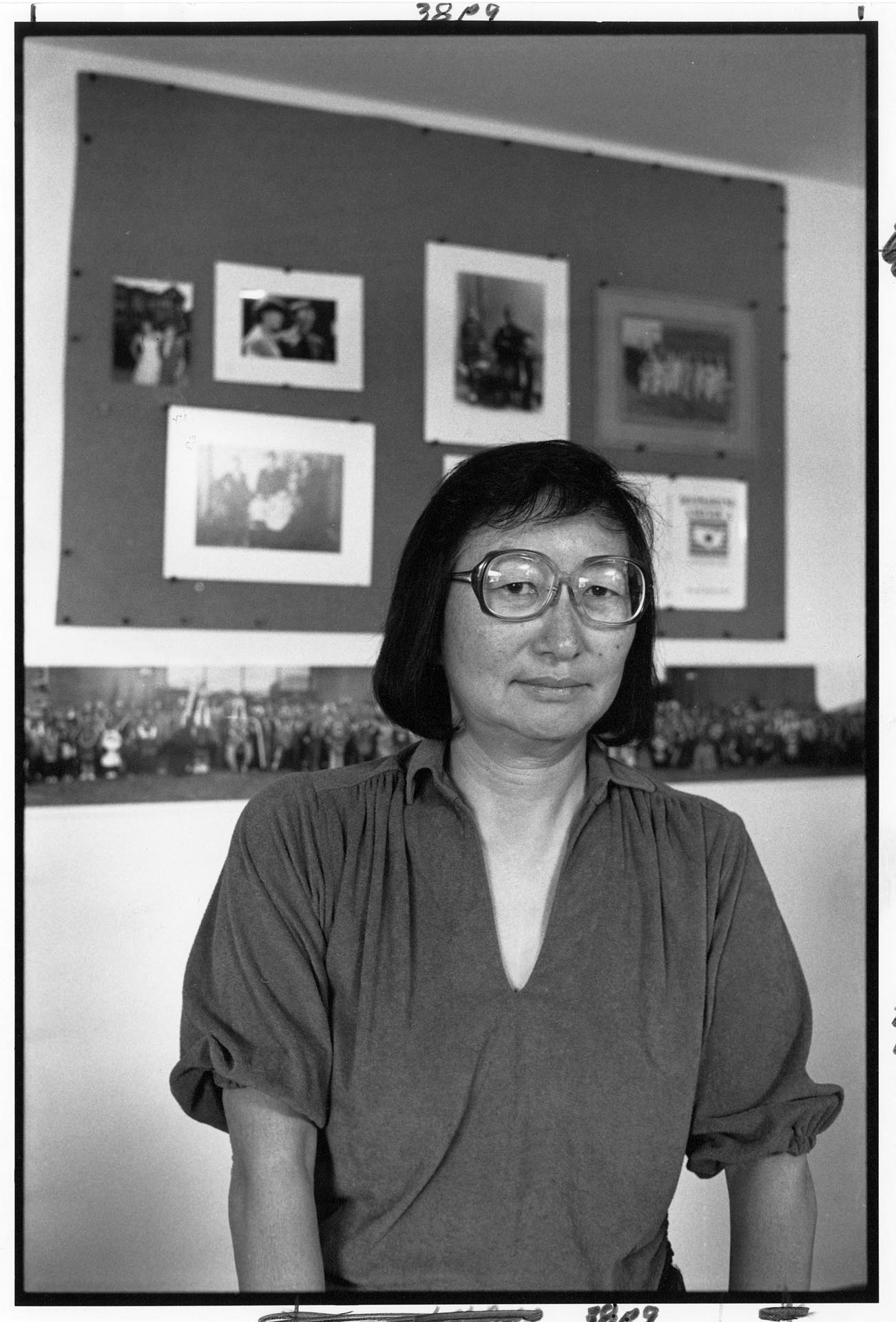 Image of Chizuko Omori at home in front of incarceration camp photos, Seattle, August 10, 1988