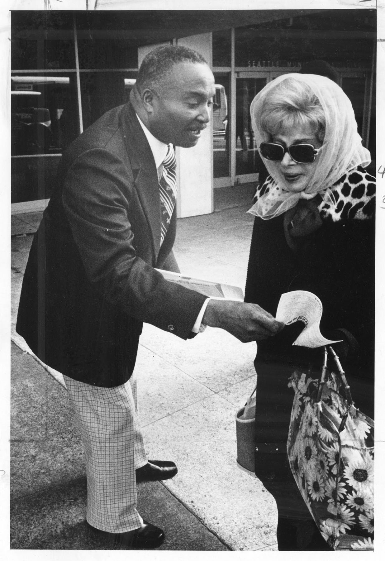 Image of Sam Smith handing woman flier on school levy, April 4, 1977