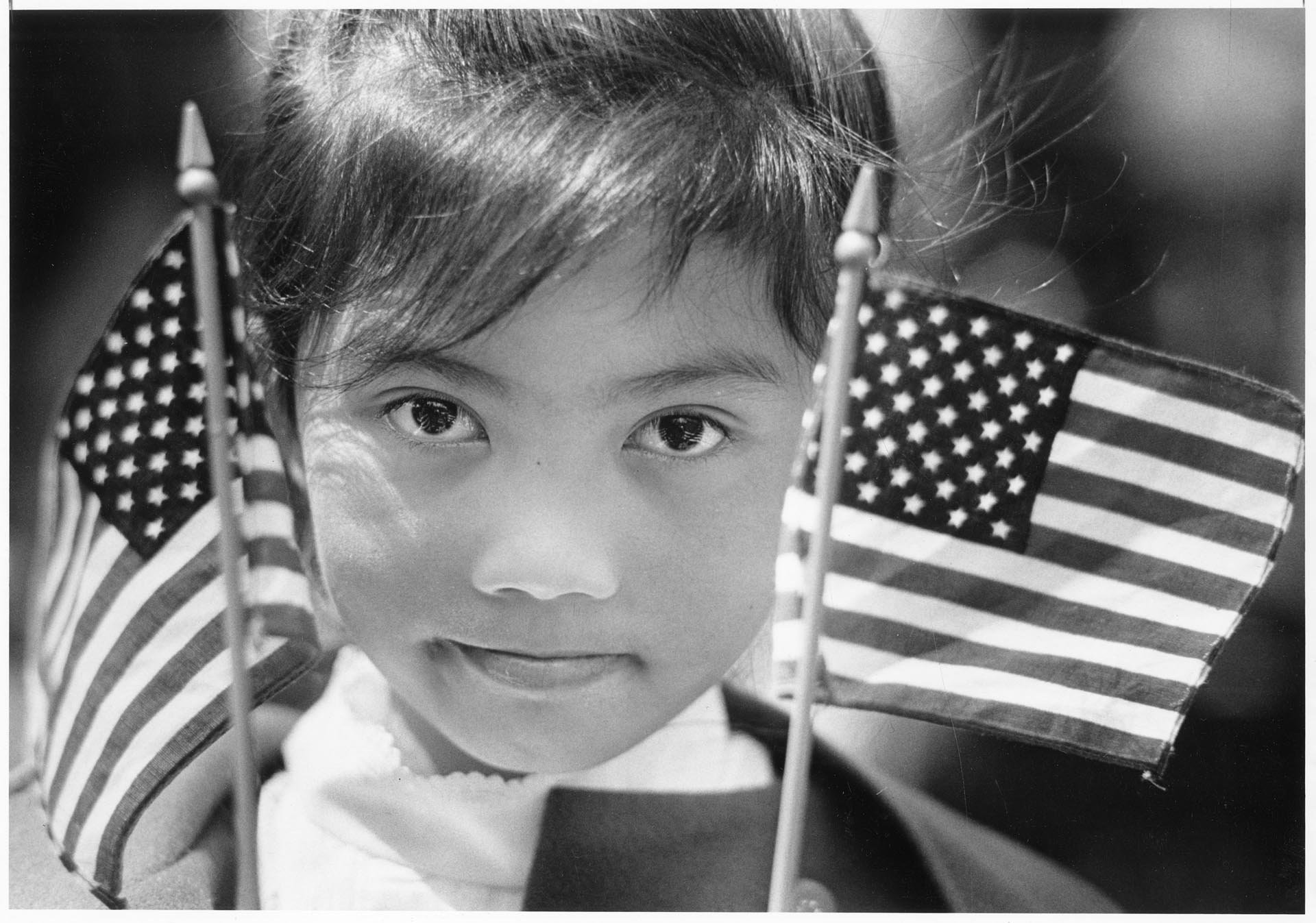 Image of Nyra Sone holding flags at U.S. citizenship ceremony at the Seattle Center, July 4, 1986