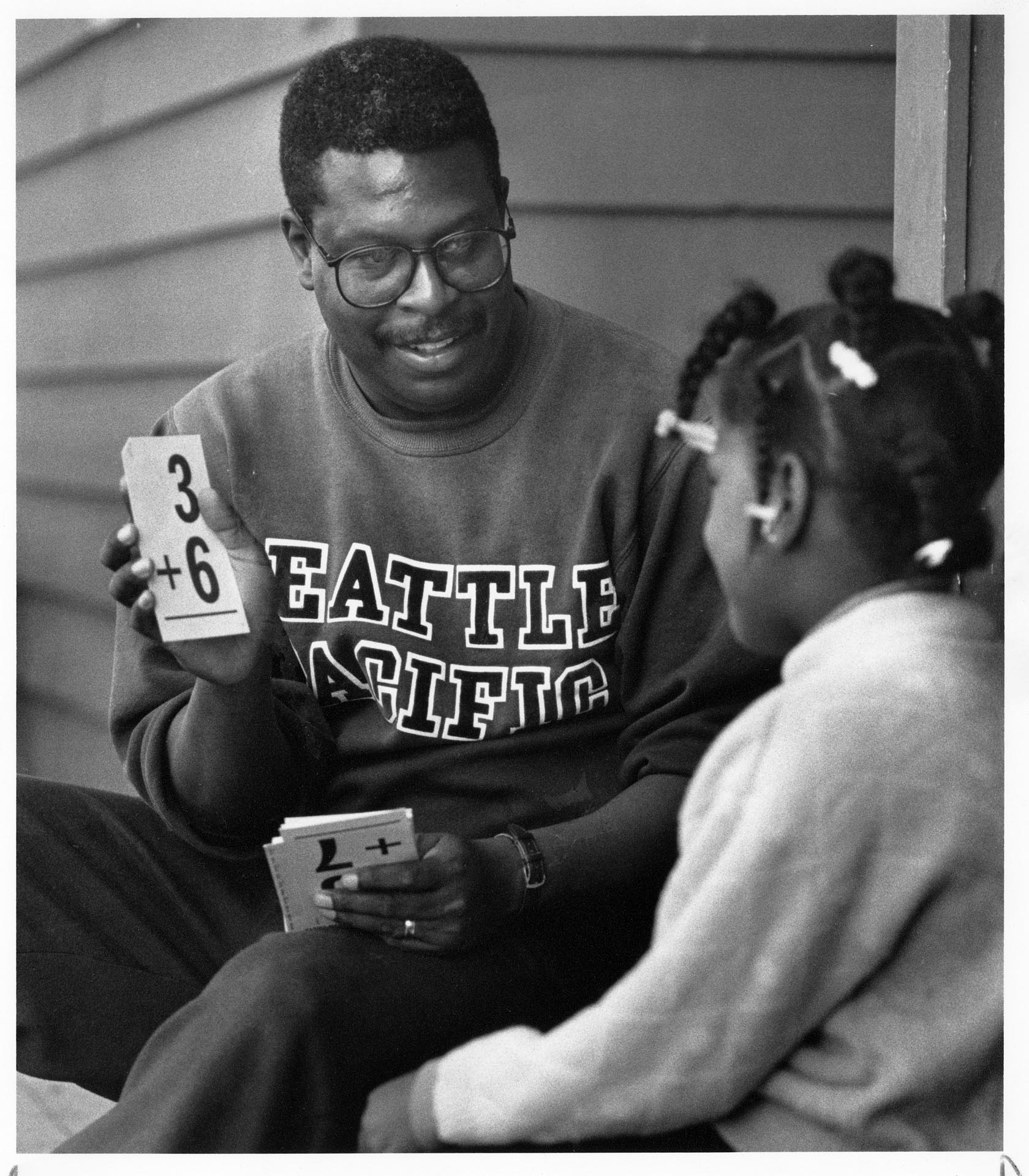 Image of Edwin Wea showing flash card to girl at Black Family Center, Seattle, October 8, 1991