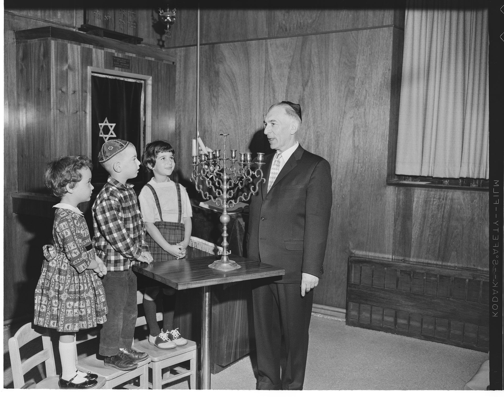 Image of Children watching rabbi light menorah candle, December 3, 1961