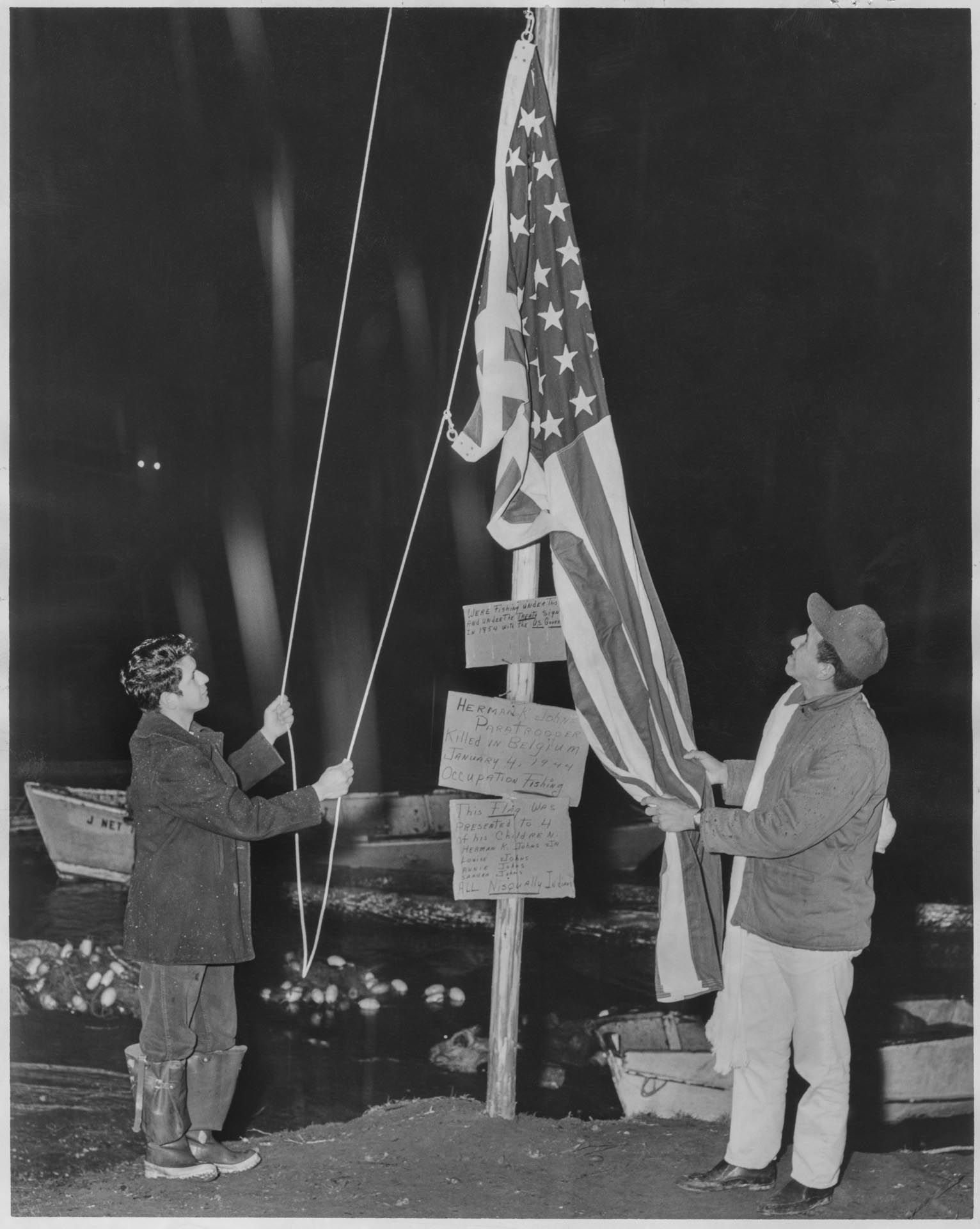 Image of Herman K. Johns Jr. and Billy Frank Jr. lower U.S. flag at protest fishing site, Frank's Landing, Nisqually River, January 21, 1964