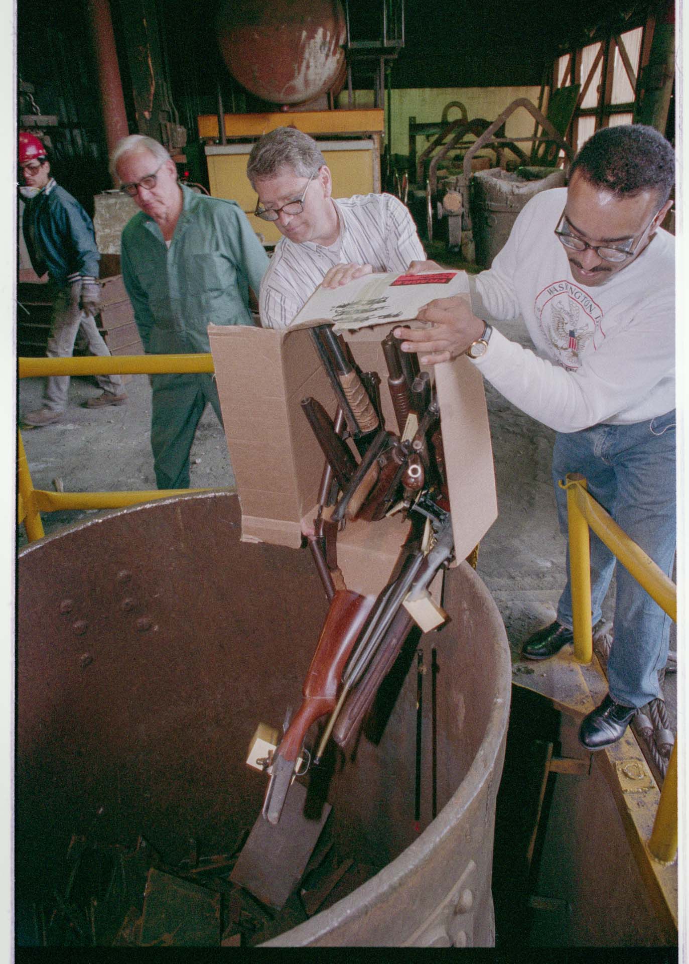 Image of Men dumping box of guns into foundry crucible, Seattle, June 16, 1993