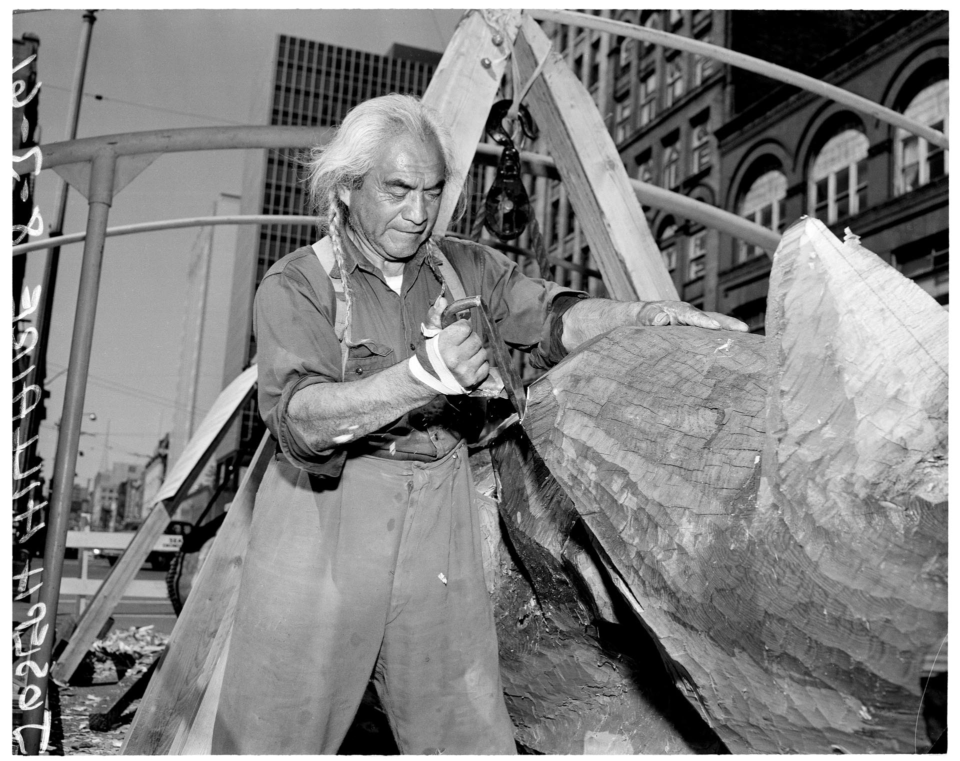 Image of Joseph Hillaire (Kwul-kwul'tw) carving totem pole in Pioneer Square, Seattle, August 3, 1961