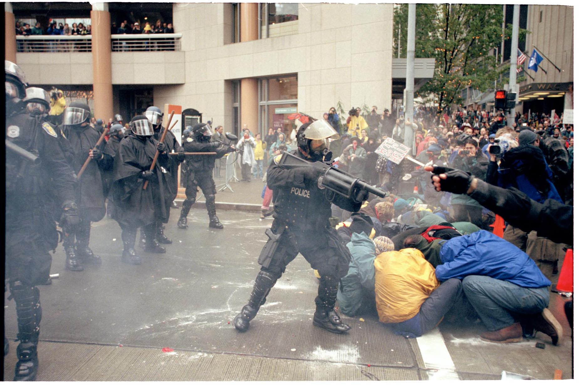 Image of Police officer pointing gas launcher at protesters at WTO protest, Seattle, November 30, 1999