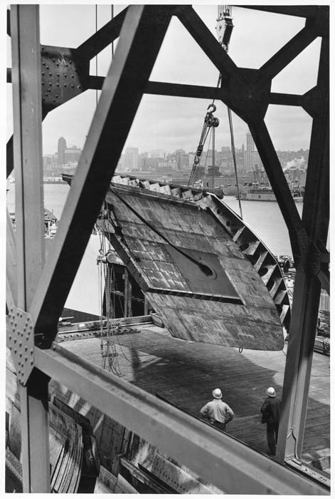 Image of Men watching large section being lifted by a crane at Todd Pacific Shipyards, Seattle Division, circa 1945