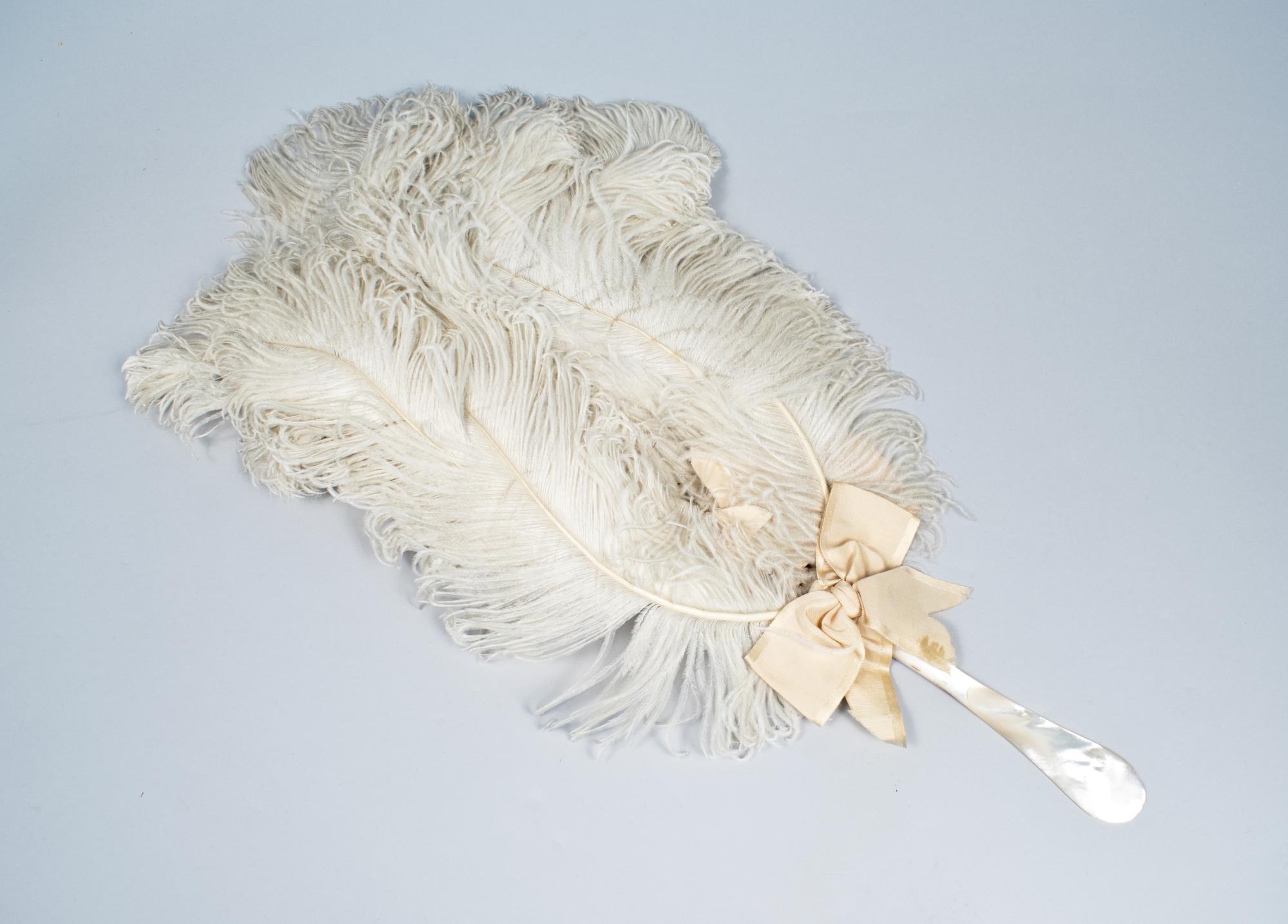 Image of White ostrich fan with mother of pearl handle, ca. 1900