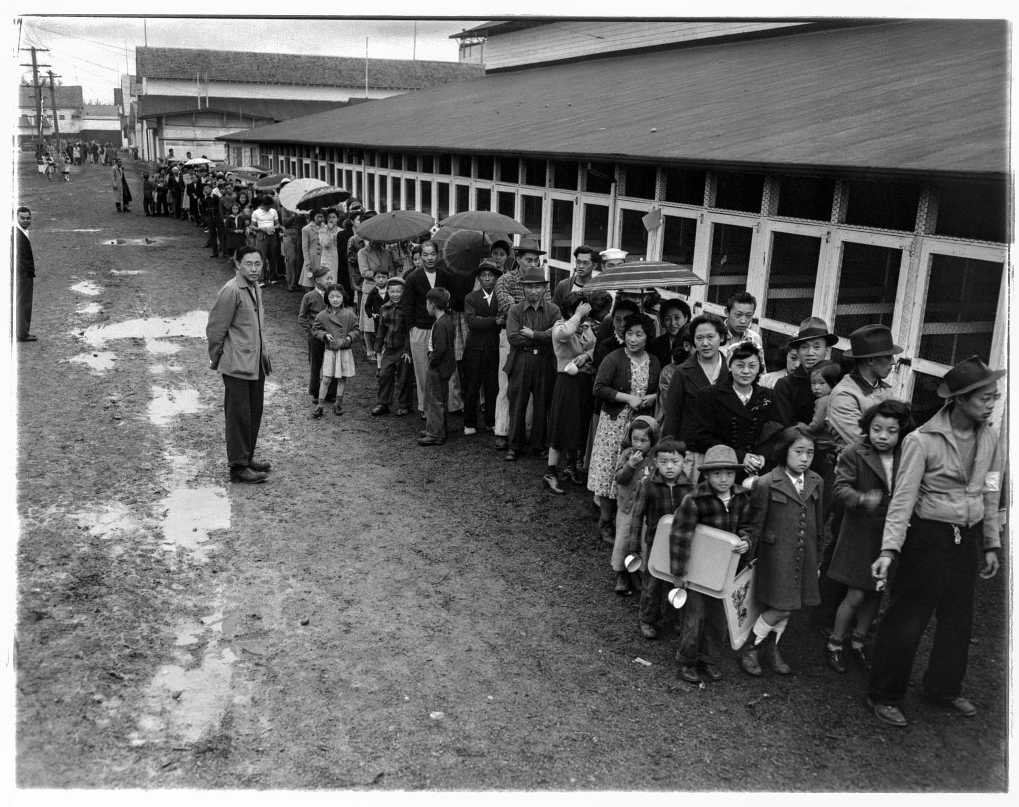 Image of Incarcerees lined up in the rain at the Puyallup Assembly Center, Puyallup, 1942