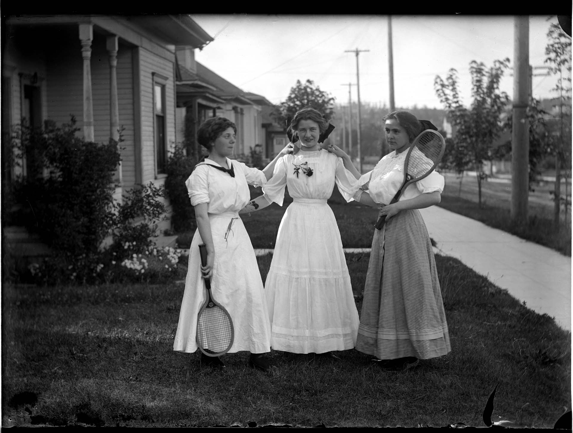 Image of Three women in front yard with tennis rackets, circa 1900