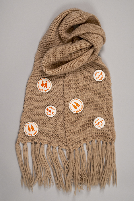 Image of Knit scarf with a collection of HJR 61 buttons attached, ca. 1972