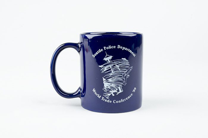 Image of Coffee mug featuring the WTO conference in a cyclone, given as gift from the Seattle Police Department to conference worker, L.A. McNeal, 1999
