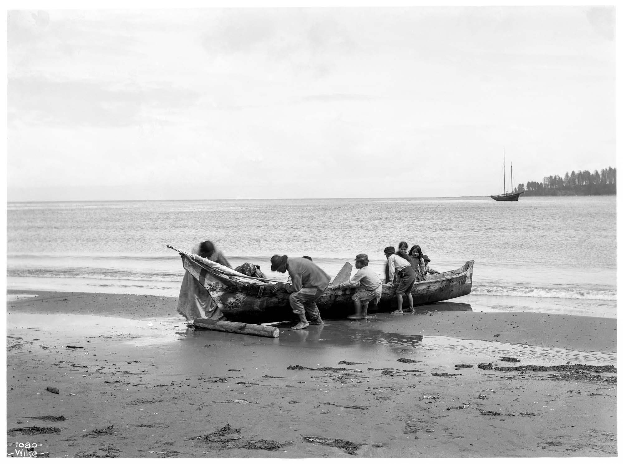 Image of Makah group pulling a canoe on shore at Neah Bay, circa 1900