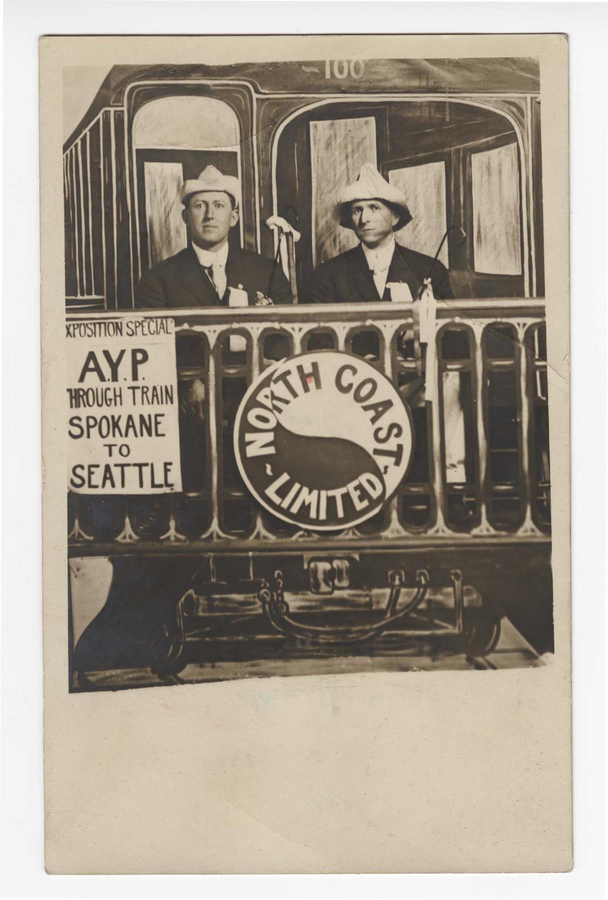 Image of Two men with train backdrop at the Alaska-Yukon-Pacific Exposition, Seattle, 1909