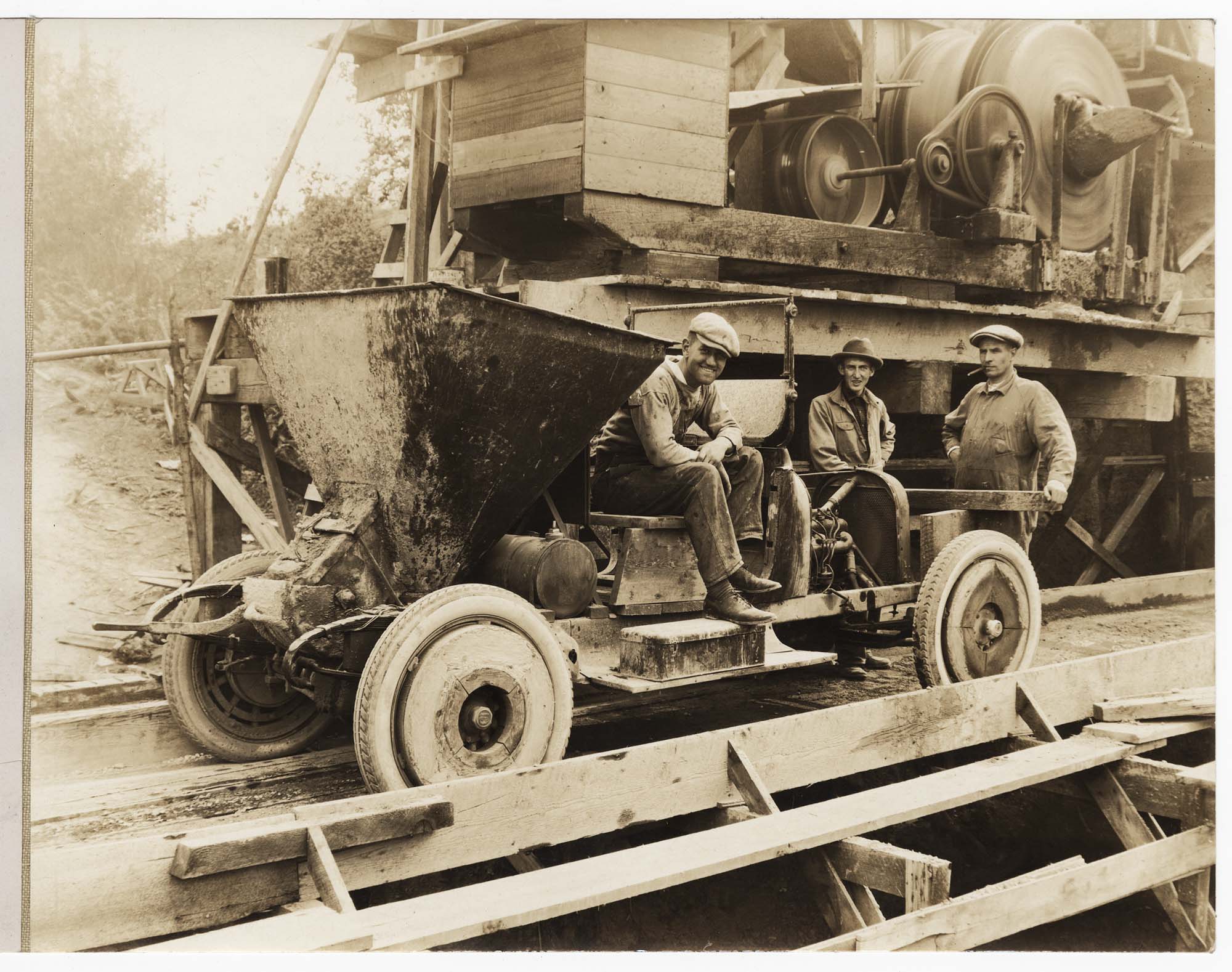 Image of Three men near concrete mixer and concrete transport car, circa 1925