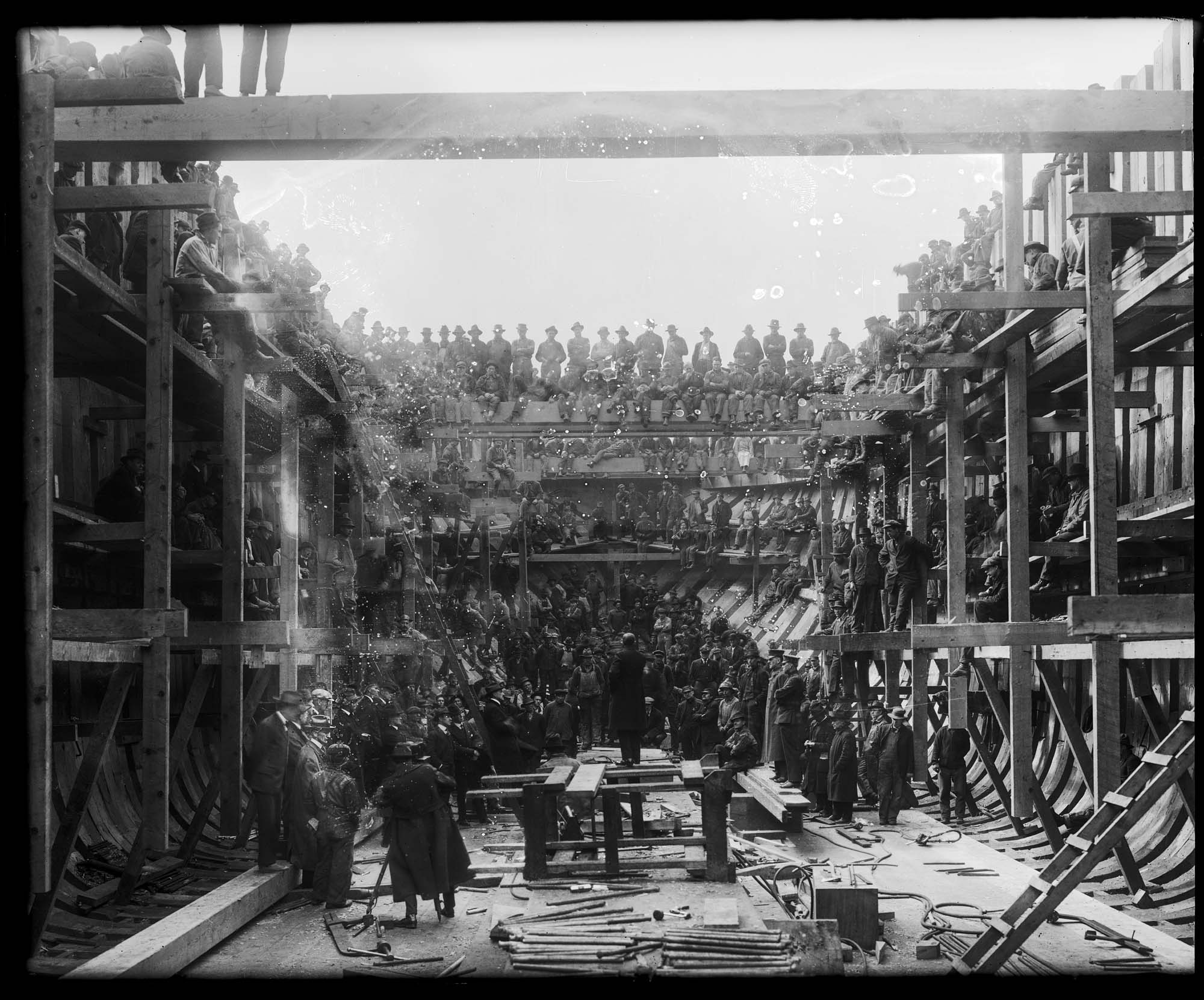 Image of Thomas Barker talking to shipyard workers inside the hull of a wooden ship, 1918