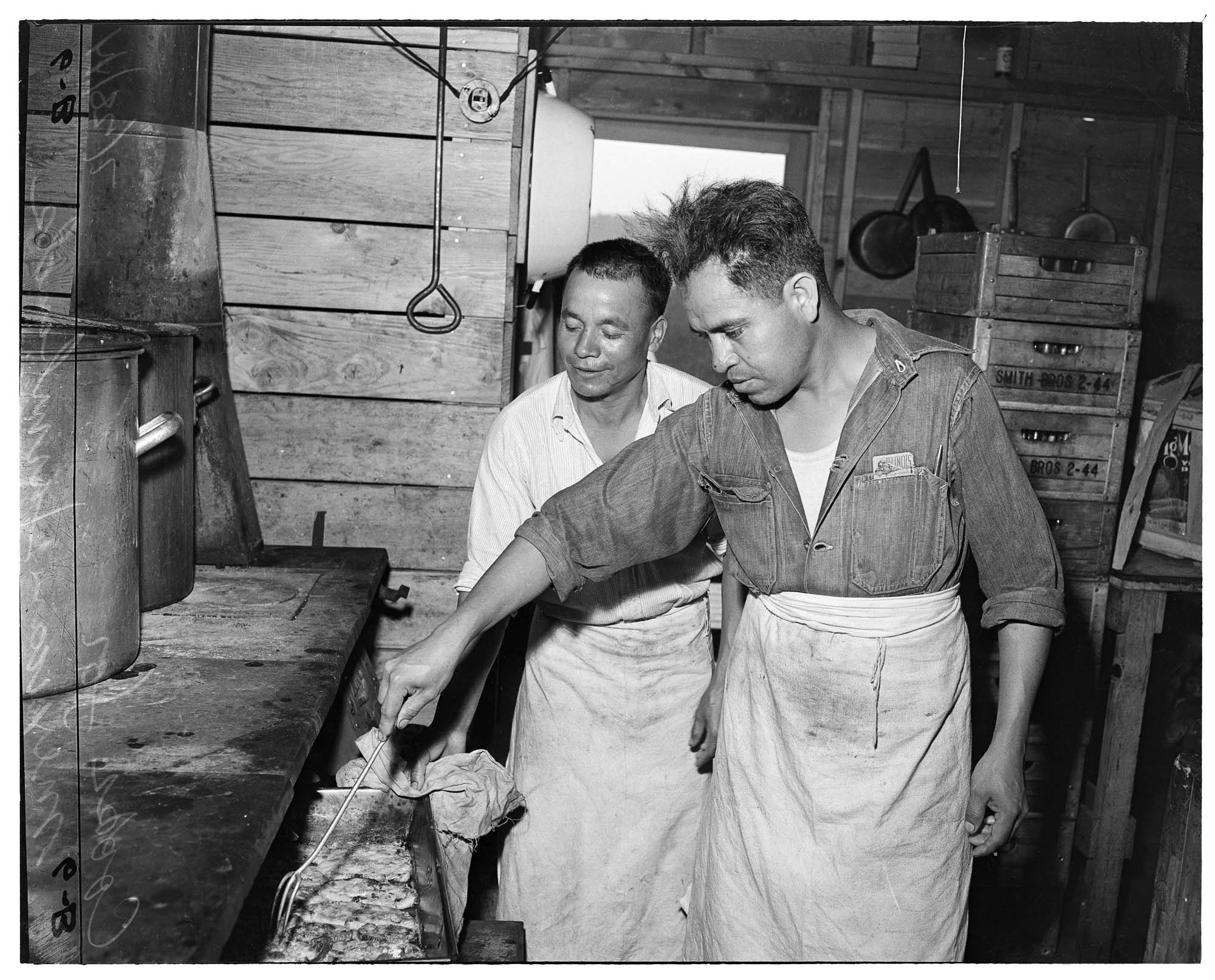 Image of Two men cooking in a kitchen of migrant camp, 1944