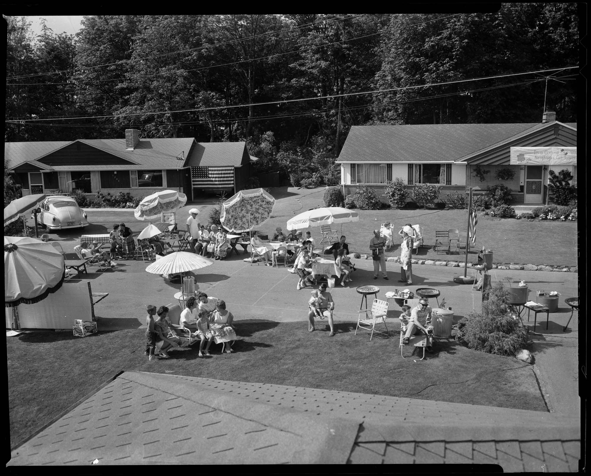 Image of Fourth of July party on NW 120th Street showing neighbors meeting in the street seen from the roof of a nearby house, Seattle, 1961