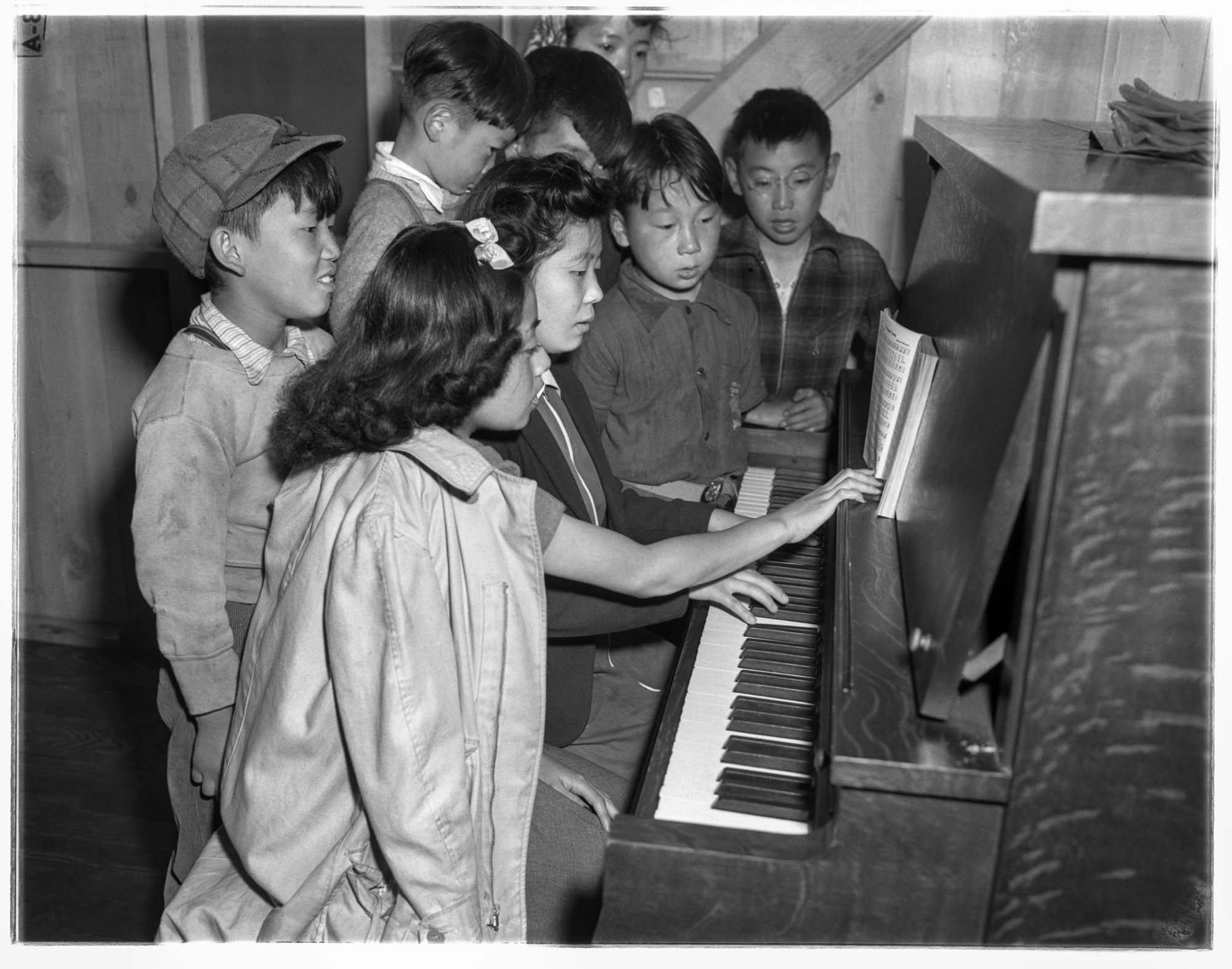Image of Teenage incarcerees gather at a piano, Puyallup Assembly Center, Puyallup, 1942