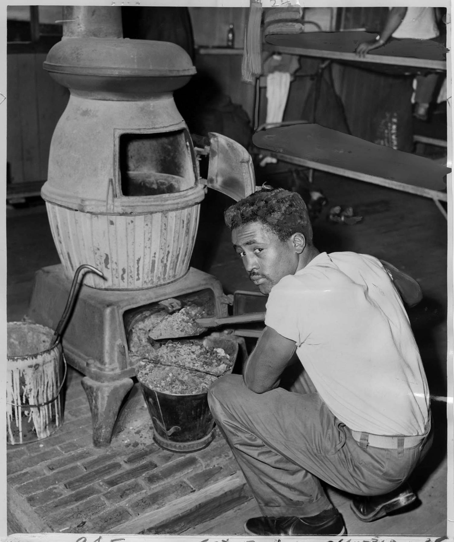 Image of Sgt. Melvin Boykin cleaning ashes from stove, Fort Lawton, July 1952