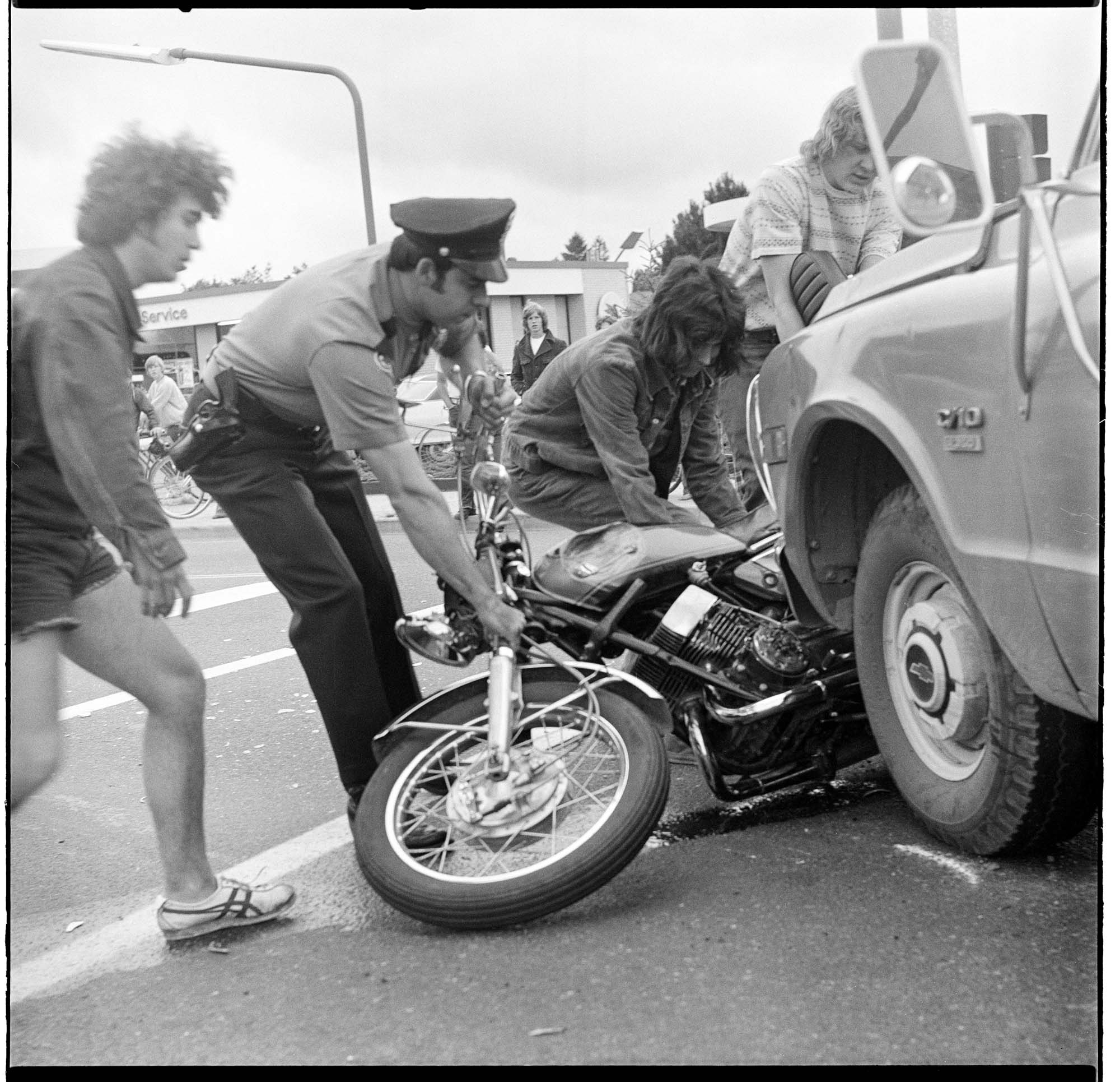 Image of Policeman and citizens removing a motorcycle from under a truck, June 25, 1974