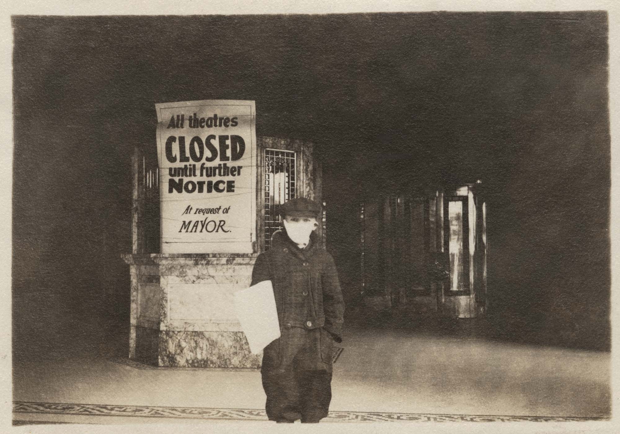 Image of Newspaper boy with mask standing in front of closed theatre 