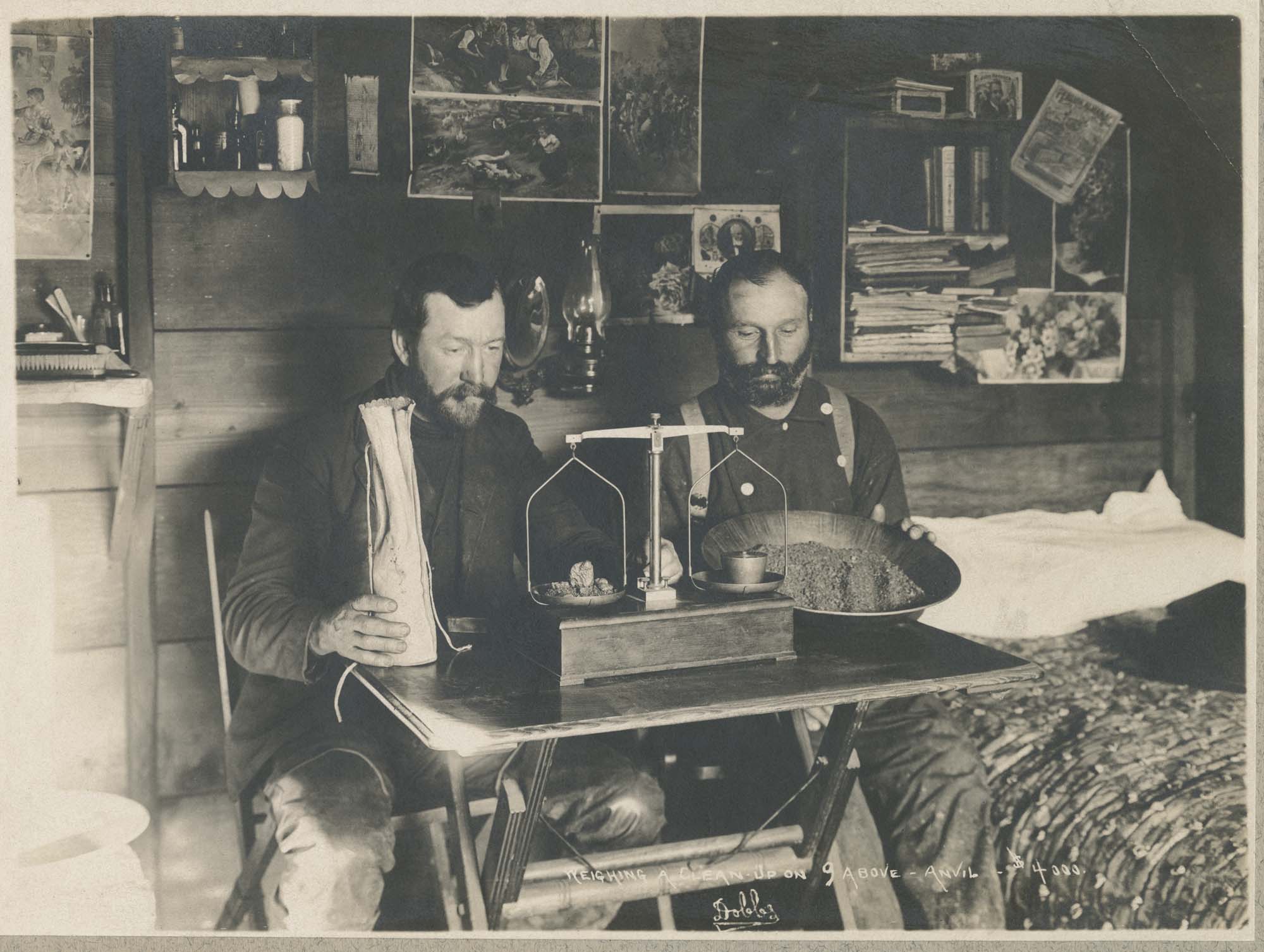 Image of Two miners weighing gold in cabin, near Nome, Alaska, circa 1900