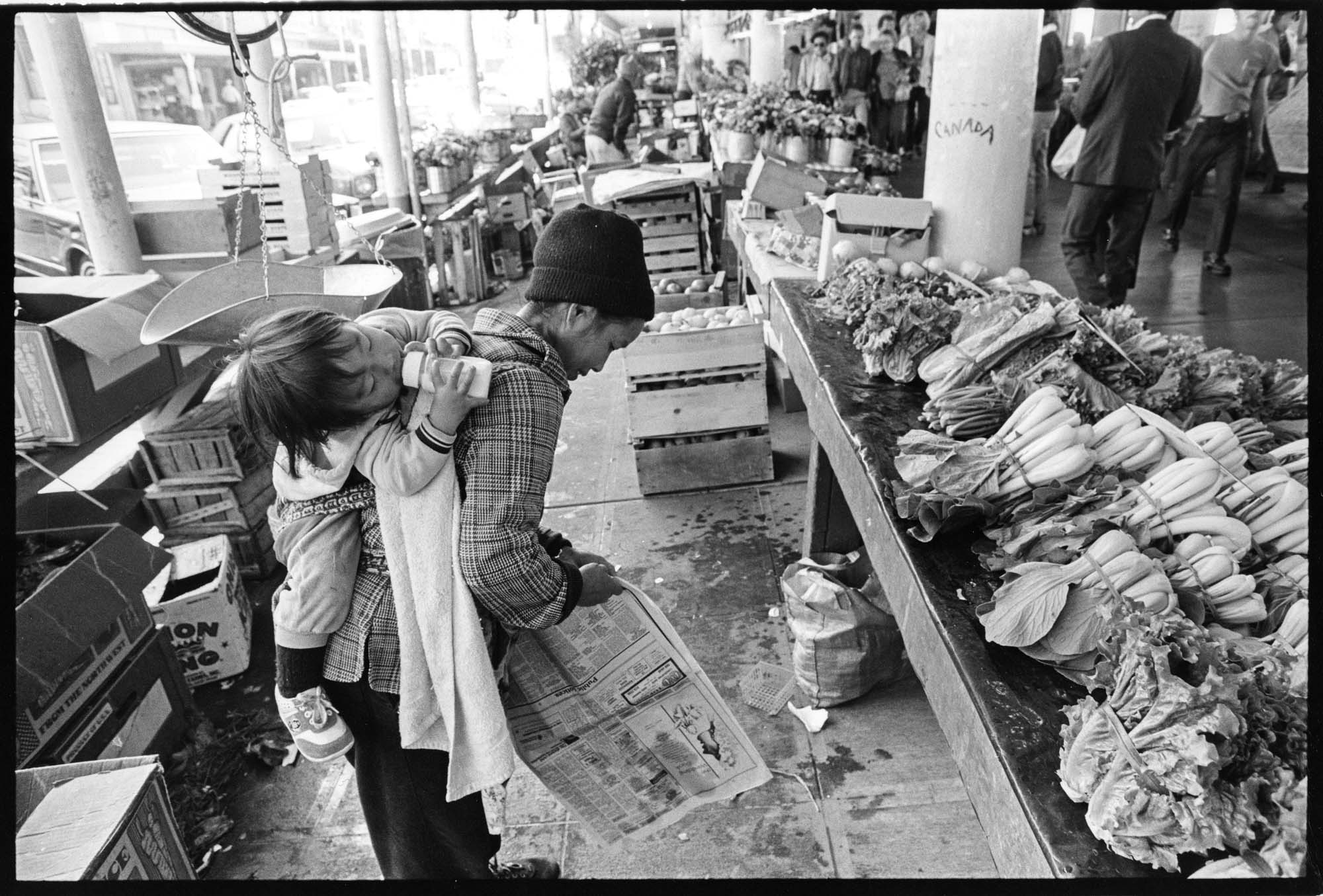 Image of Pike Place Market produce vendor carrying child on her back, Seattle, September 23, 1983
