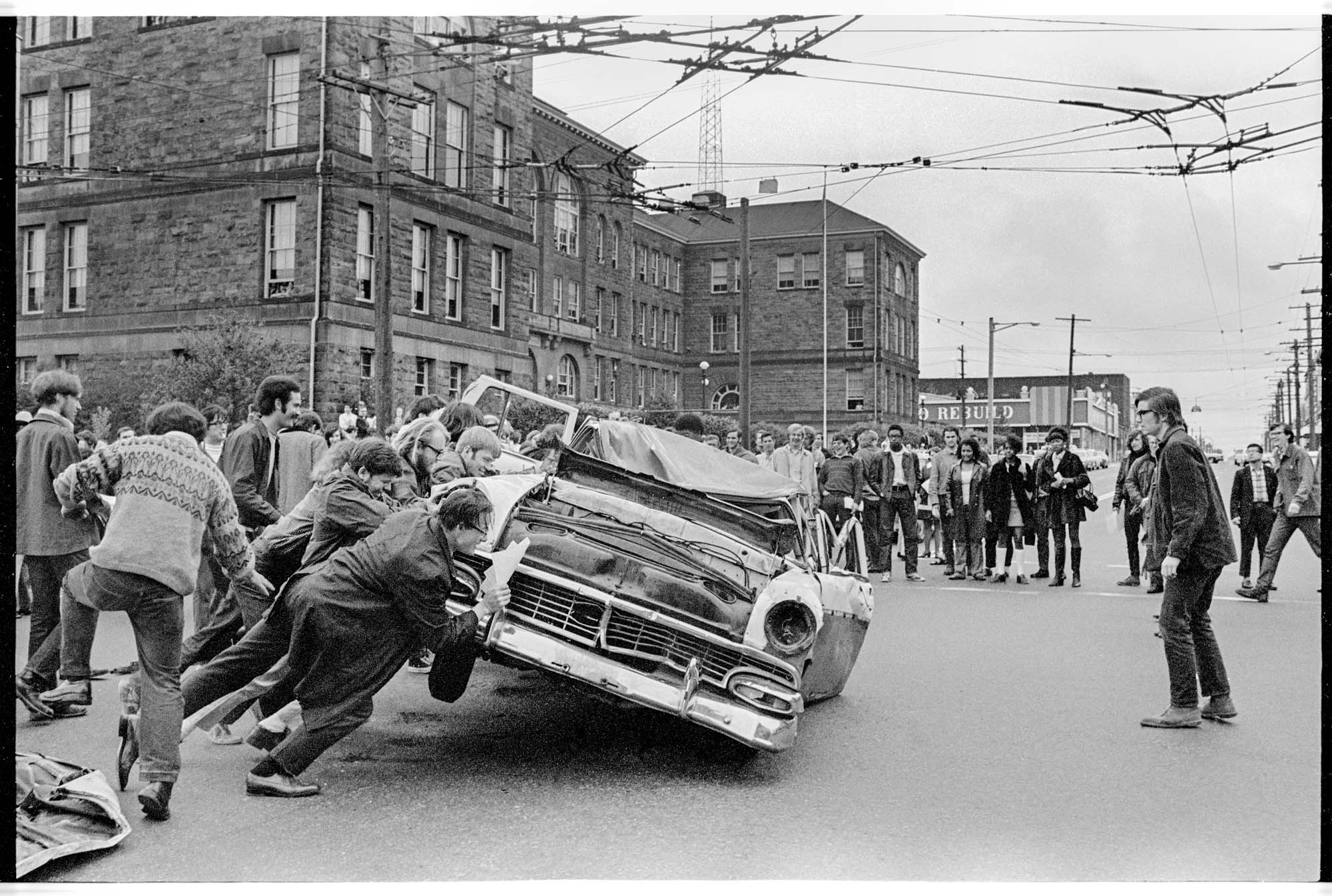 Image of Students overturning car in Earth Day demonstration outside Seattle Community College, Seattle, 1970
