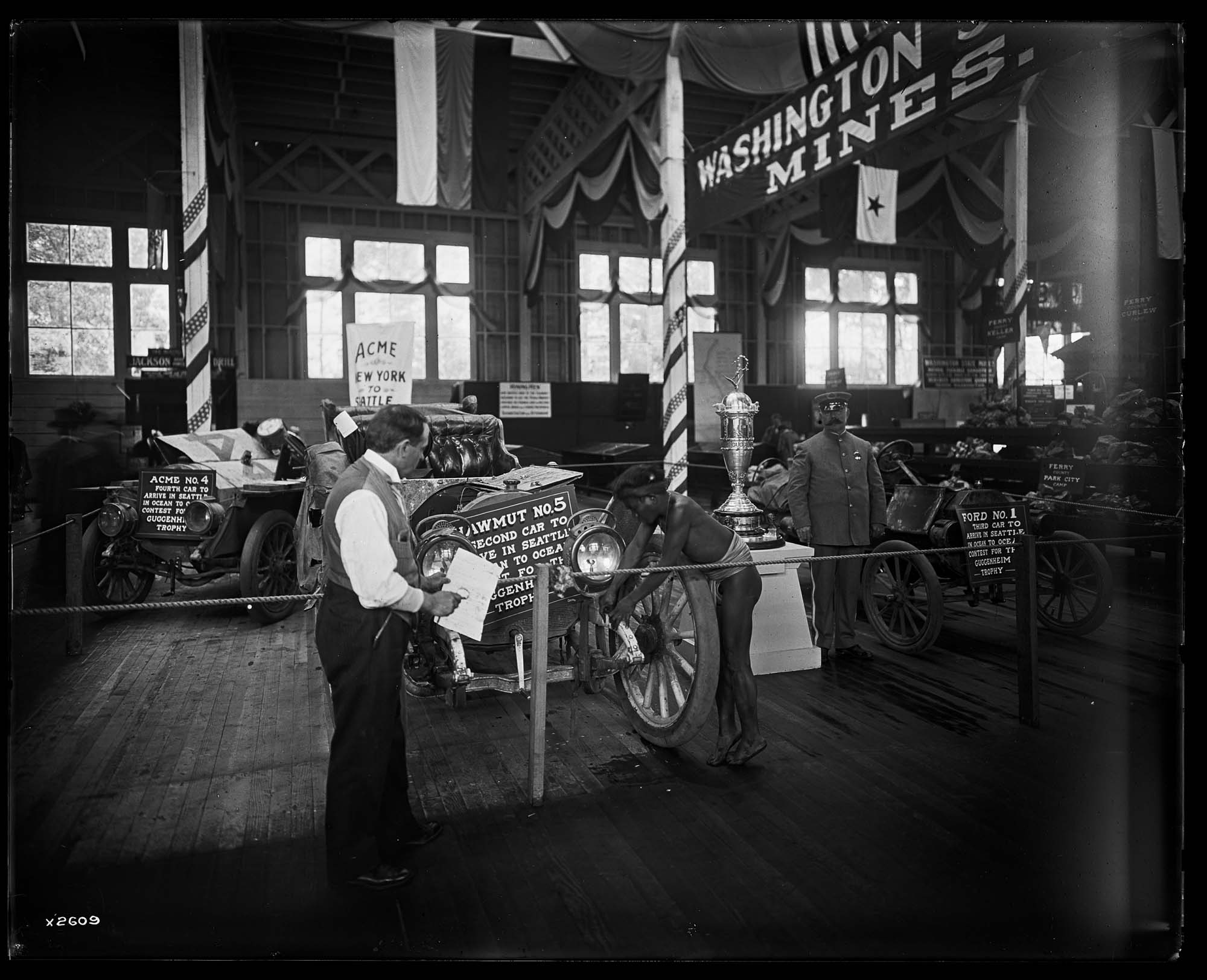 Image of Two white men and and Igorot man in car exhibit, Alaska-Yukon-Pacific Exposition, Seattle, 1909