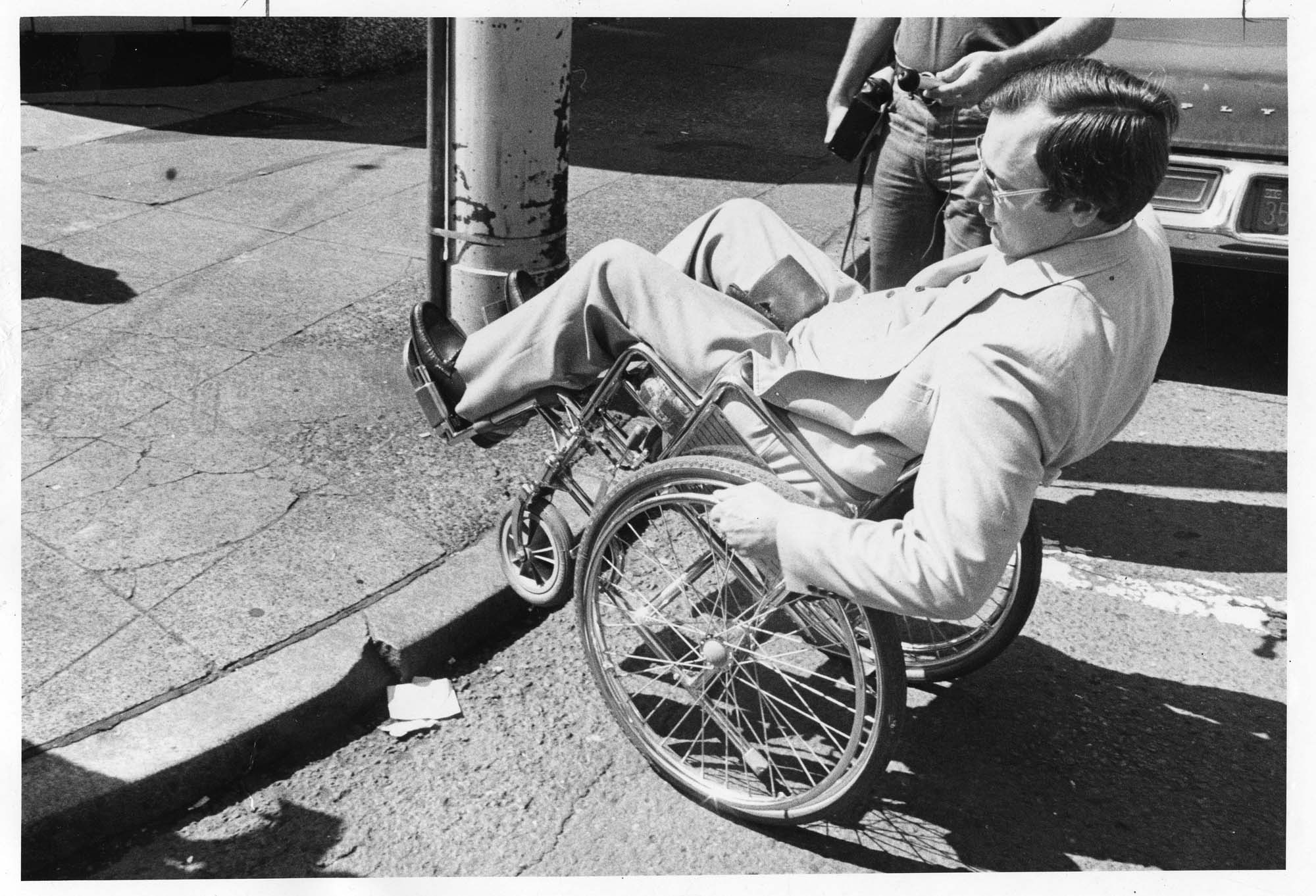 Image of Mike Kovell demonstrating that curbs can be a barrier for people in wheelchairs, Seattle, July 1978