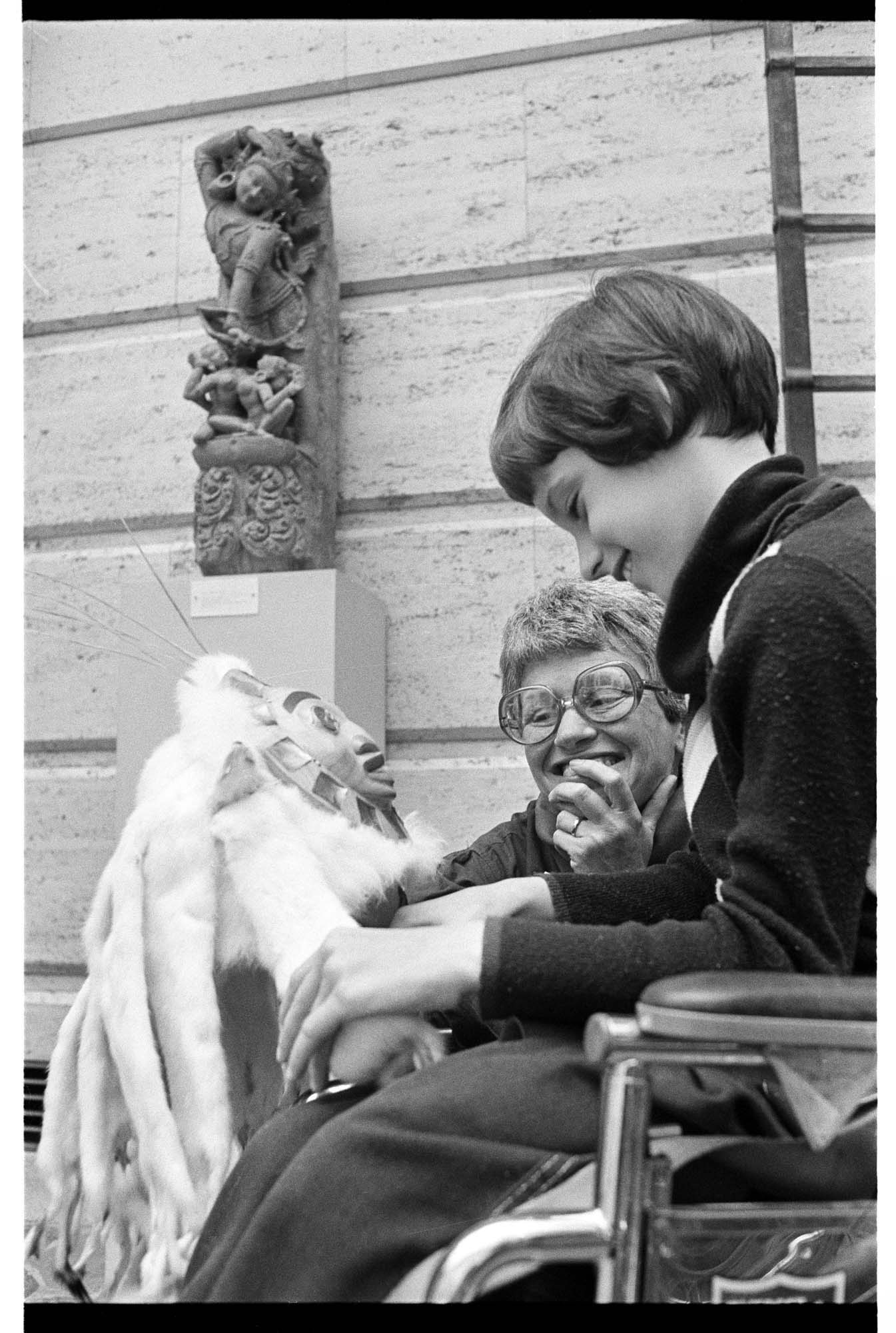 Image of Docent Evelyn Klebanoff showing Indian mask to child in wheelchair, May 24, 1977