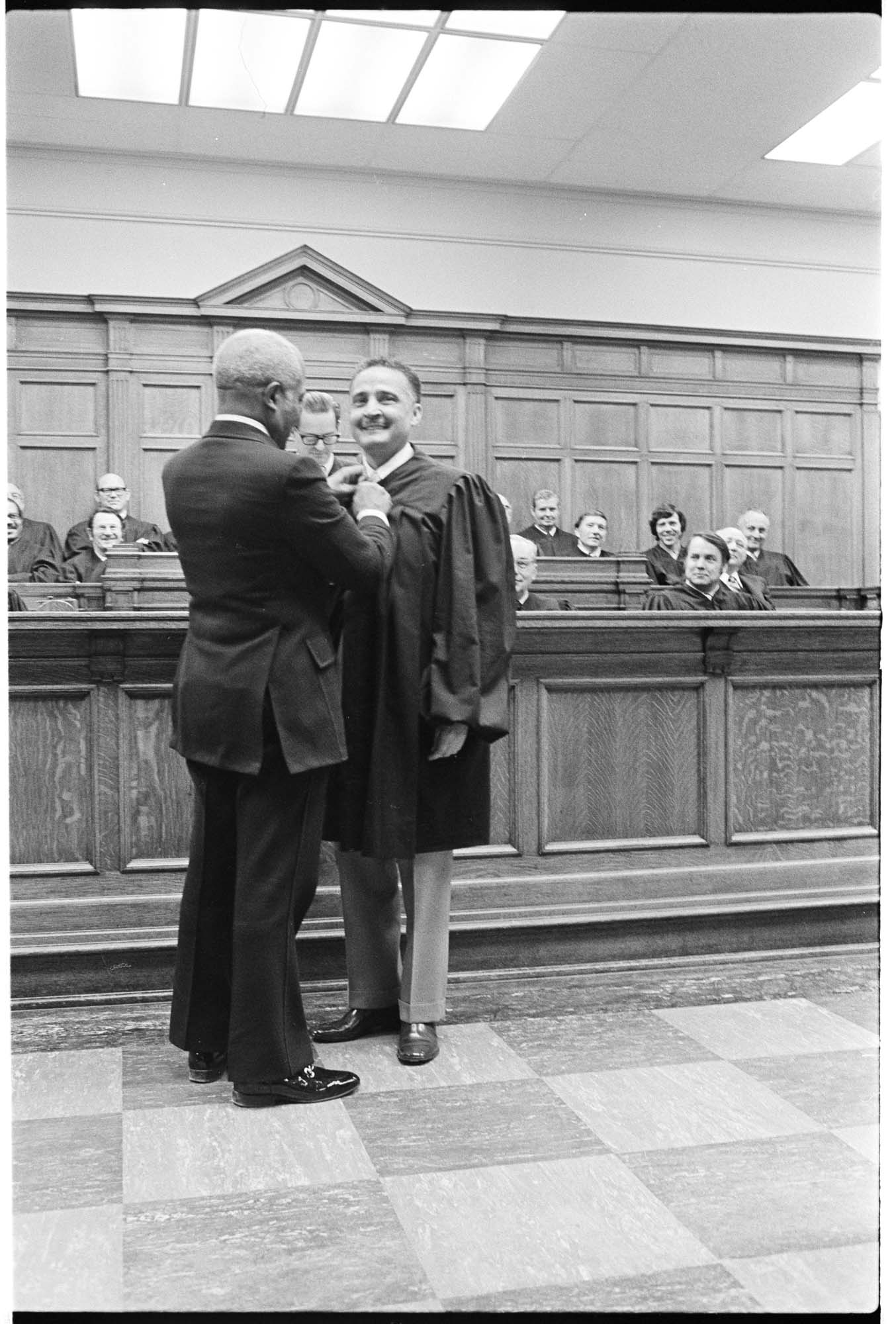 Image of Charles Stokes helping Herbert Stephens with his robes at swearing-in ceremony, March 8, 1974