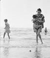 Image of Mildred Mar carrying child at beach, Des Moines, circa 1960