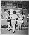 Image of Three women looking at photographs on exhibit, Seattle, circa 1950