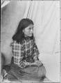 Image of Young Indigenous woman named Tasha seated by a tent, circa 1900