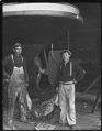 Image of Two men in front of ship hull holding flag, probably in Seattle, circa 1910