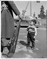Image of Japanese American boy standing near a soldier with a rifle, possibly in Seattle, 1942
