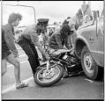 Image of Policeman and citizens removing a motorcycle from under a truck, June 25, 1974